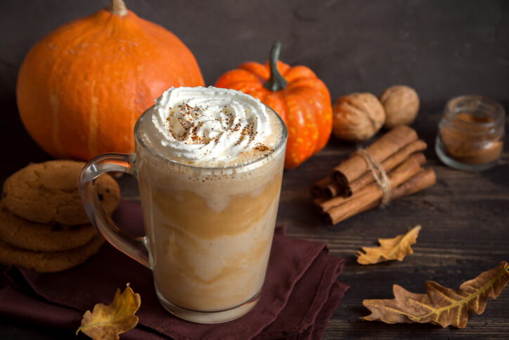 Das Herbstgetränk Pumpkin Spice Latte im Vordergrund, mit Kürbissen im Hintergrund