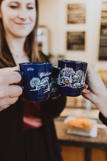 Drei Frauen auf einem Weihnachtsmarkt am anstoßen mit Glühwein. Man sieht die Tassen in Großaufnahme