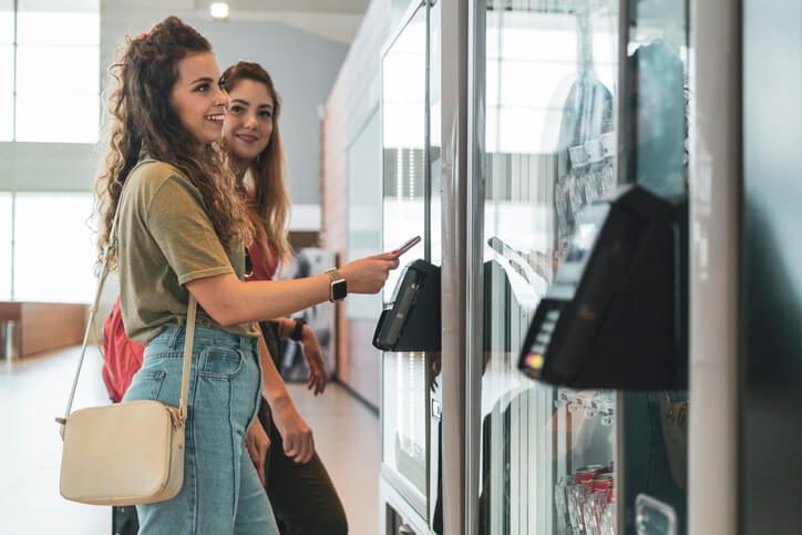 zwei Frauen gehen in einem 24/7 Laden zusammen einkaufen. Sie bezahlen gerade an einem Automaten mit der Karte.