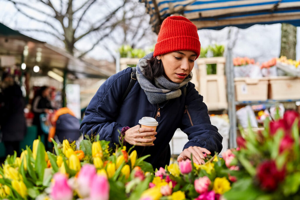 Frau mit einem Kaffee in der Hand auf einem der Frühlingsmärkte in Bamberg. Sie stöbert zwischen bunten Tulpen. 