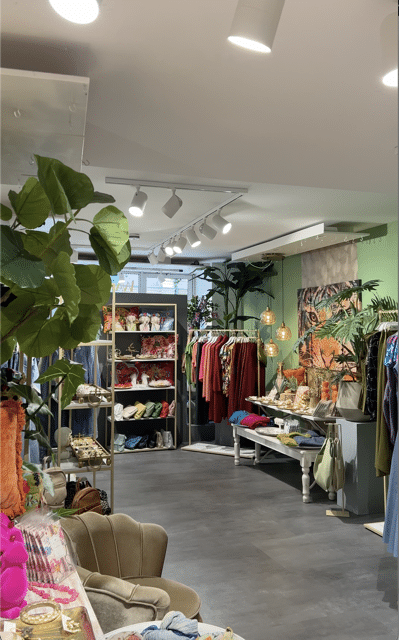 Ein Bild vom Geschäft Wanka Tonka von innen mit Regalen und Kleiderstangen im Hintergrund und Pflanzen und Schmuck im Vordergrund.