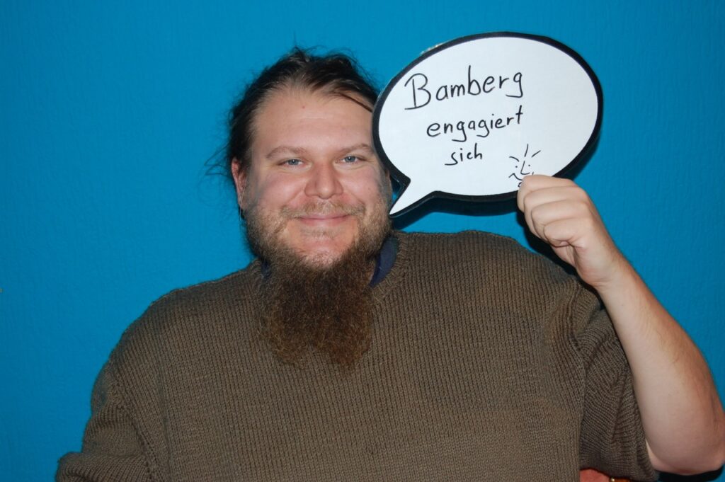 Ein ehrenamtlicher Mitarbeiter des Freiwilligenzentrums CariThek Bamberg hält ein Schild mit "Bamberg engagiert sich" hoch.